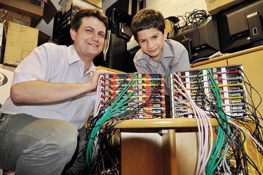 Description: Professor Cox and his son with a cluster of Pis that link together to form a supercomputer